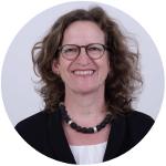 Eine Frau mit Locken und Brille lacht in die Kamera