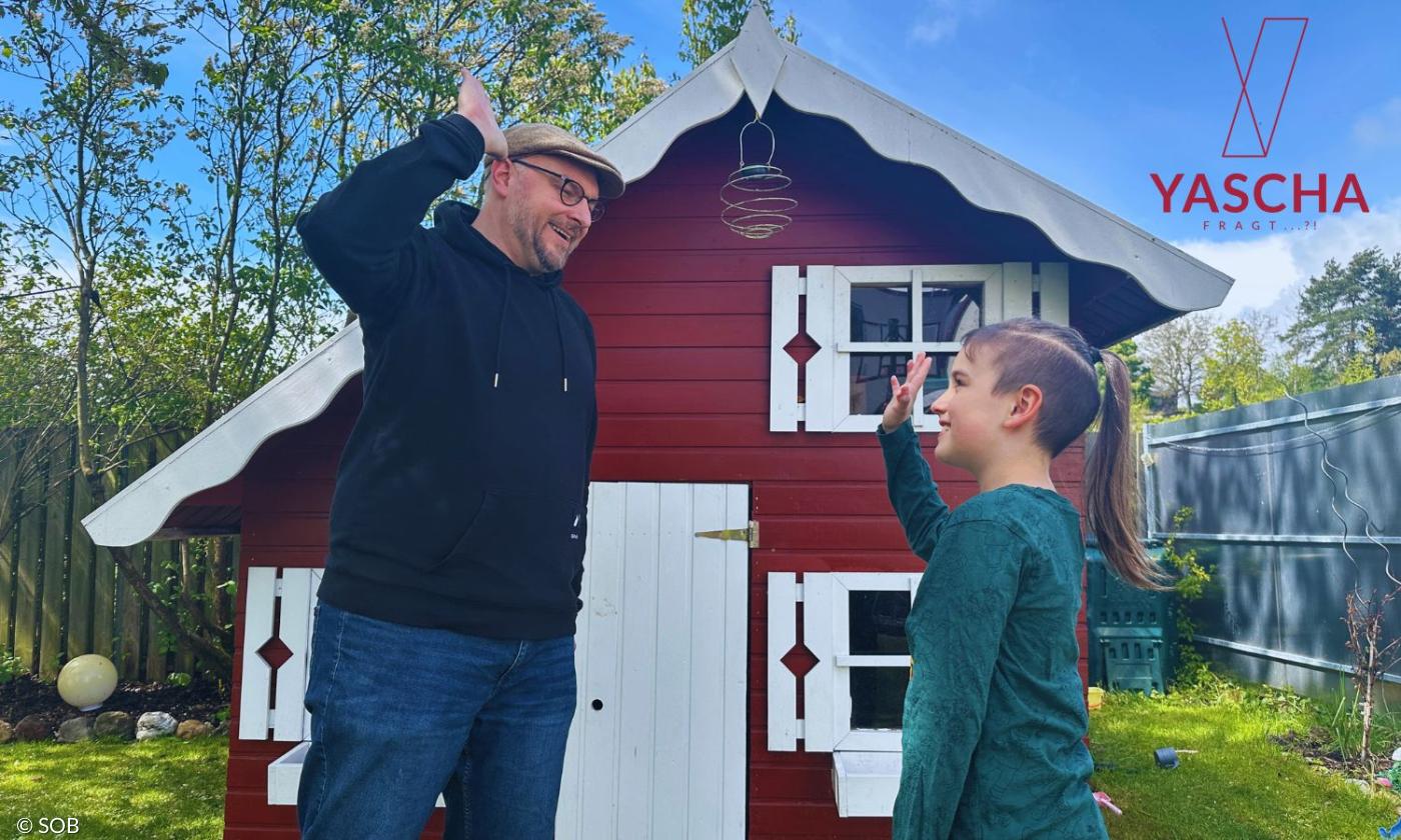 Ein Junge und ein Mann vor einer Gartenhütte, sie geben sich High Five