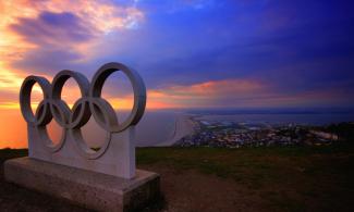 Die olympischen Ringe aus Beton. Sie tronen über einer Stadt. Die Sonne geht gerade auf.