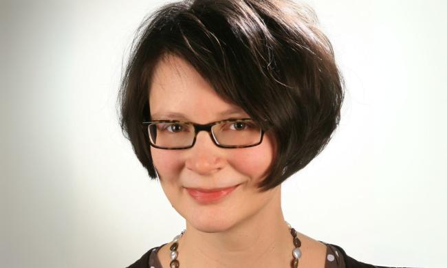Eine Frau mit braunen Haaren und Brille, sie lächelt