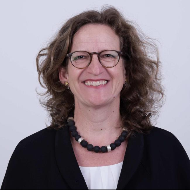 Eine Frau mit Locken und Brille lacht in die Kamera