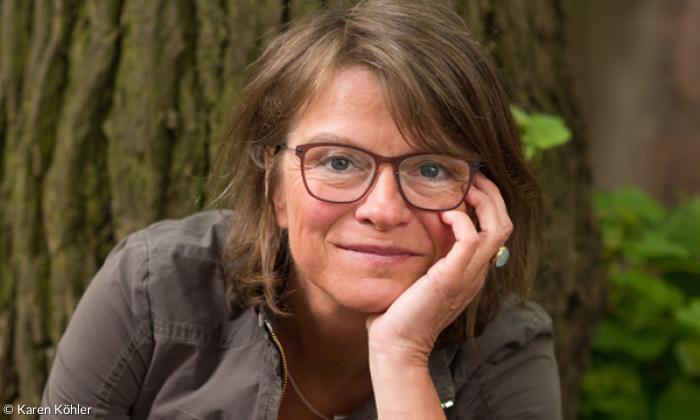 Eine Frau, hinter ihr ein Baumstamm