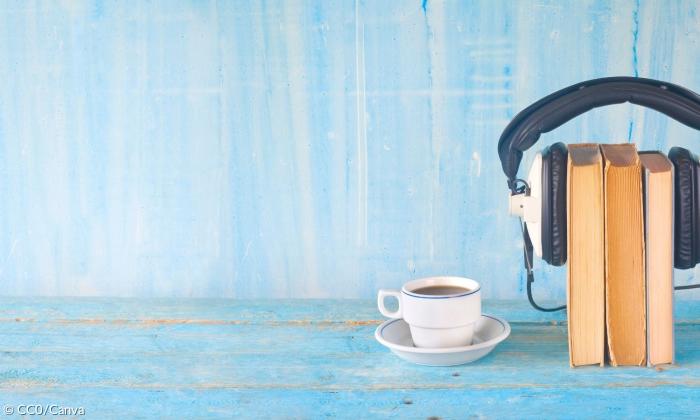 Eine Tasse Kaffee mit Untertasse. Daneben drei Bücher mit Köpfhörern. 