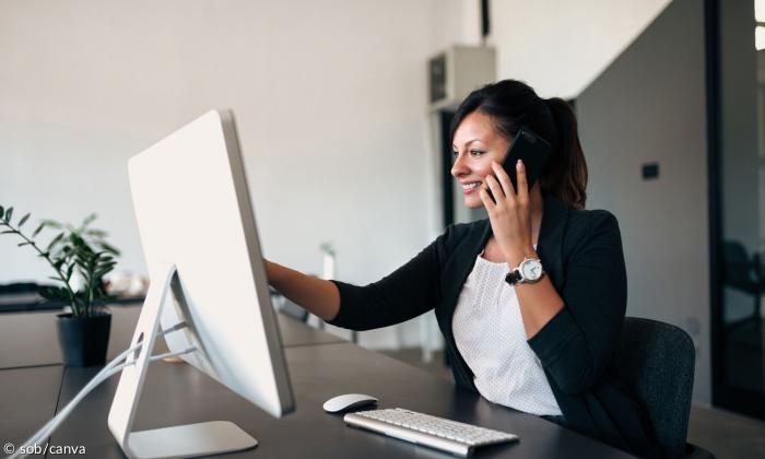 Eine Frau sitzt am Computer, während sie telefoniert.
