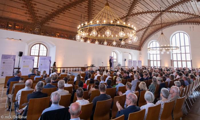 Menschen sitzen auf Stühlen und schauen zum Rednerpult