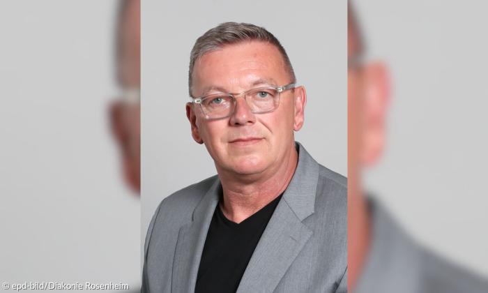 Ein Mann Mitte vierzig, der ein graues Sakko trägt, blickt frontal in die Kamera. 