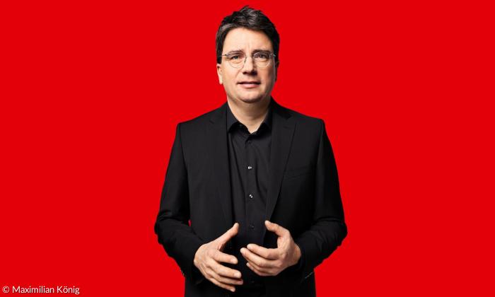 Ein Mann in schwarz gekleidet vor einem roten Hintergrund