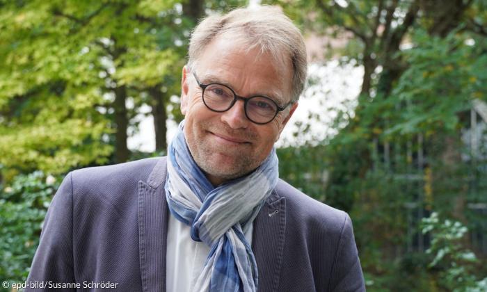 Ein Mann mit Brille und Schal, er lächelt