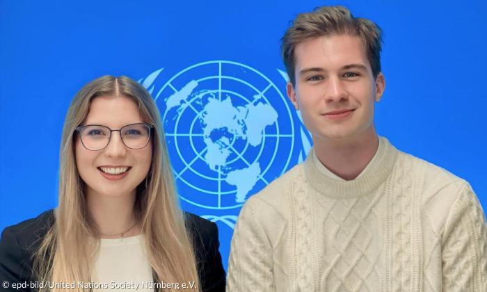 Eine junge Frau und ein junger Mann vor dem UN-Logo