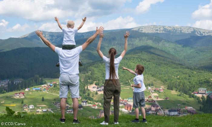 Eine vierköpfige Familie steht auf einem Berg und hebt die Arme in die Luft