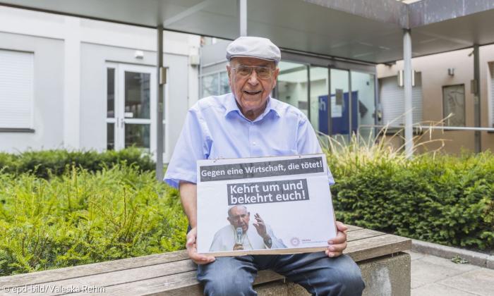 Ein Mann mit einem Schild, auf dem der Papst zu sehen ist, dazu die Schrift: "Gegen eine Wirtschaft, die tötet! Kehrt um und bekehrt euch!"