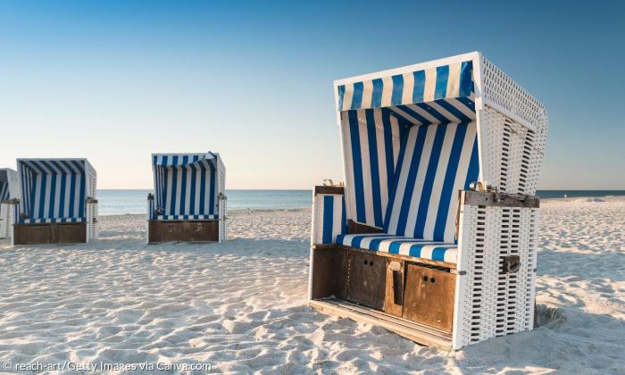 Strandkörbe an einem Sandstrand, dahinter das Meer