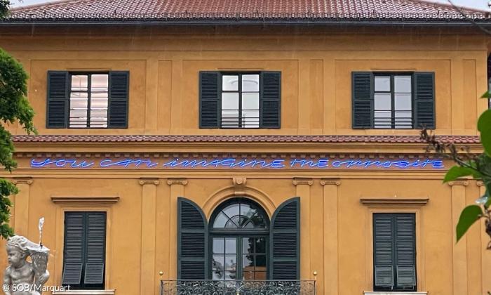 Leuchtschrift an einem Haus "You can imagine the opposite"