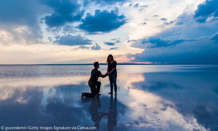 Ein Mann kniet vor einer Frau, scheinbar auf dem Wasser, dahinter Wolken und ein Abendhimmel