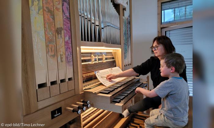 Ein Kind sitzt an einer Orgel, eine Frau steht neben ihm