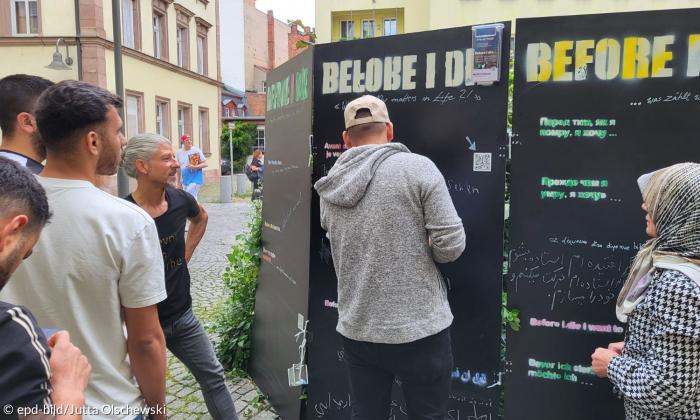 Mehrere Menschen stehen vor einer schwarzen Wand, auf der groß "Before I die" steht