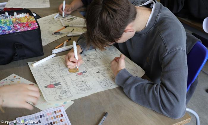 Ein Junge malt auf einem Blatt Papier und beugt sich dabei darüber