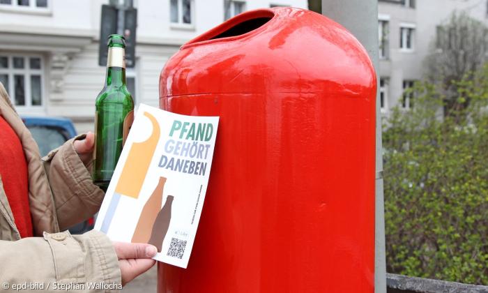 An einem roten Mülleimer klebt ein Schild mit Pfand gehört daneben. 