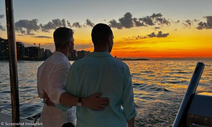 Zwei Männer schauen Arm in Arm auf einen Sonnenuntergang über dem Meer
