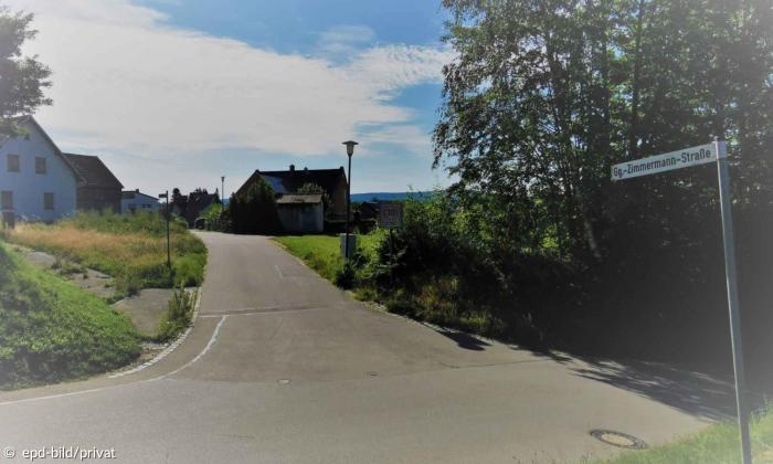 Eine ländliche Straße, an der ein Schild mit der Aufschrift "Gg.-Zimmermann-Straße" steht