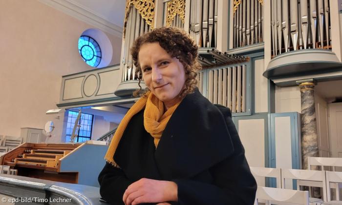 Frau mit braunen Haaren steht vor einer Orgel 