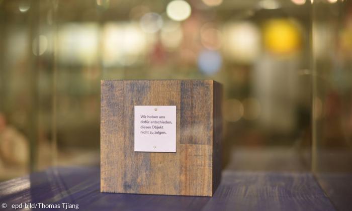 Eine Vitrine, in der ein Holzblock steht, darauf ein Schild, auf dem "Wir haben uns entschieden, dieses Objekt nicht zu zeigen" steht