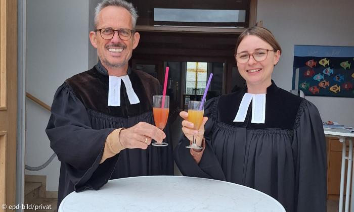 Ein Mann und eine Frau im Talar an einem Stehtisch mit Getränken in der Hand