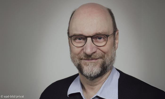 Ein Mann mit Brille und grauem Bart schaut in die Kamera