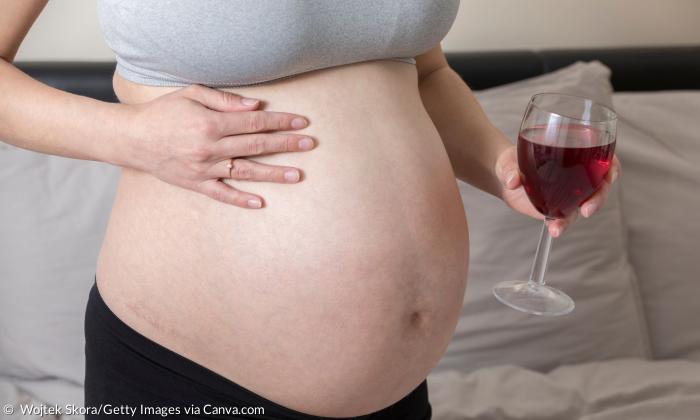 Eine schwangere Frau hält ein Glas Rotwein vor ihren Babybauch