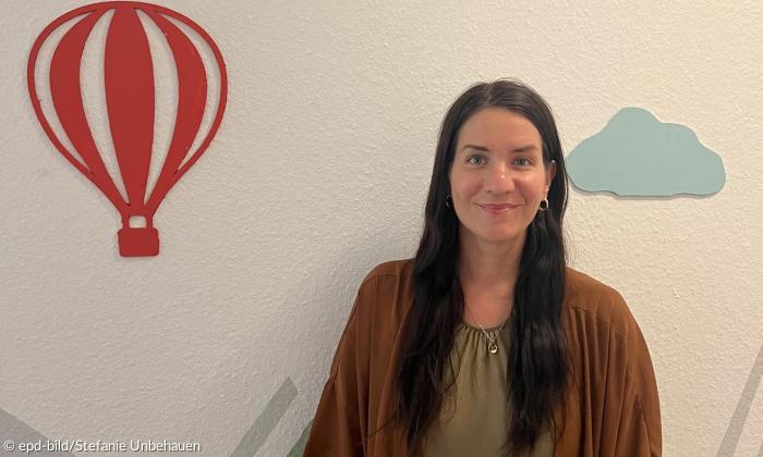 Eine Frau steht vor einer Wand, an der ein roter Heißluftballon und eine blaue Wolke angebracht sind