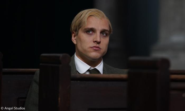Ein Mann mit blonden Haaren sitzt auf einer Kirchenbank