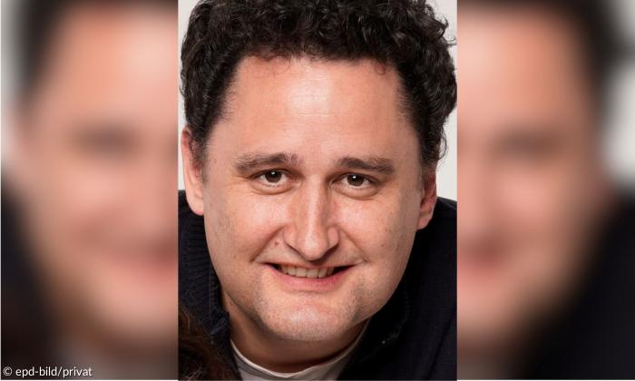 Ein Mann mit dunklen Haaren blickt in die Kamera