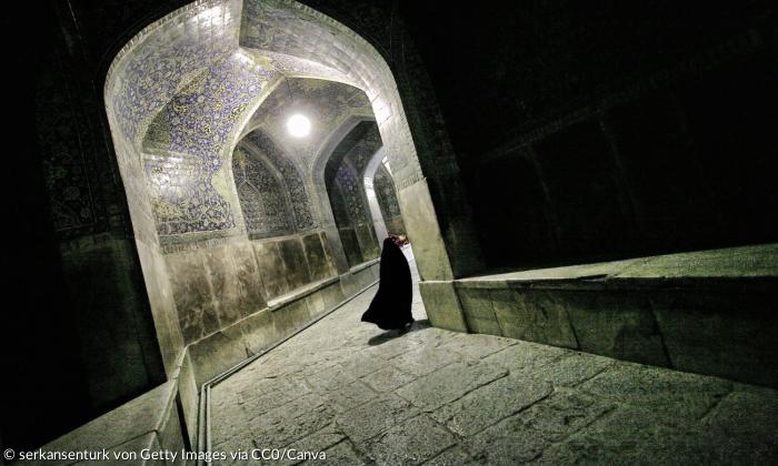 Eine ganz in schwarz verschleierte Frau geht durch einen orientalischen Gang