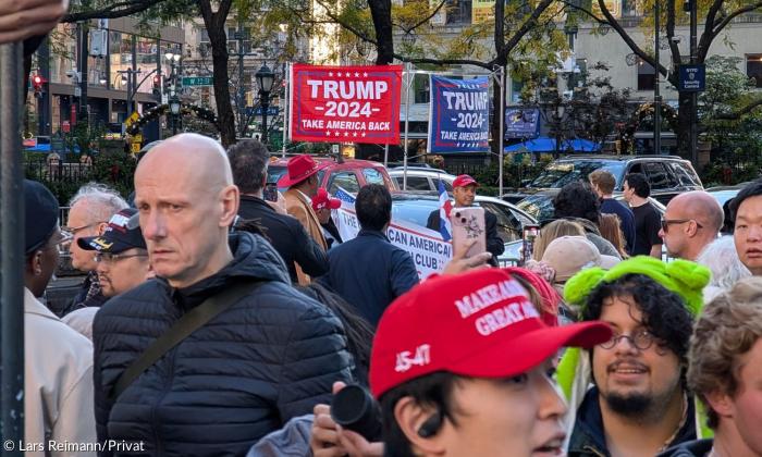 Mehrere Menschen besuchen eine Wahlkampfveranstaltung von Donald Trump und halten Schilder hoch