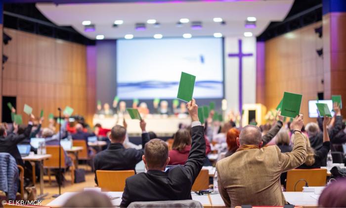 Mehrere Menschen heben grüne Karten zur Abstimmung in die Höhe