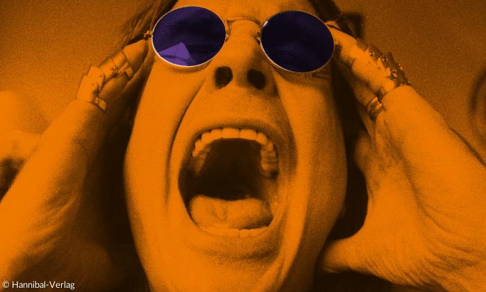 Ein Mann mit Sonnenbrille reißt den Mund auf und hält sich die Finger an die Schläfen