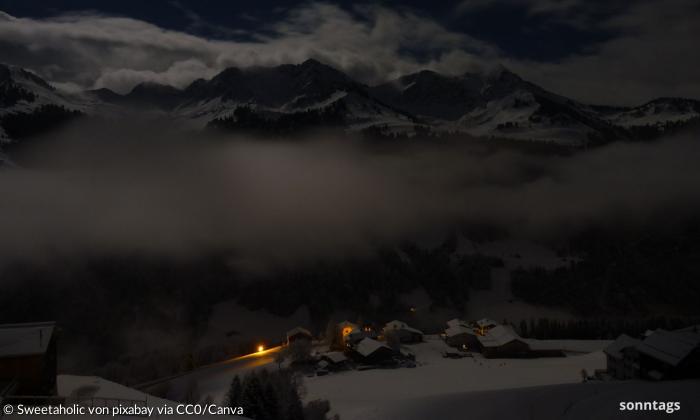 Ein Dorf in der Nacht vor wolkenumhangenen Bergen