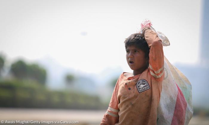 Ein Junge im schmutzigen Oberteil mit einem Sack auf dem Rücken