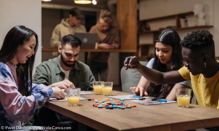 Mehrere Menschen sitzen an einem Tisch und spielen ein Brettspiel