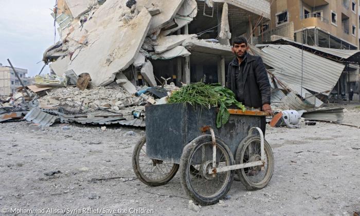 Ein Mann mit einem Wagen voller Gemüse vor zerbombten Ruinen