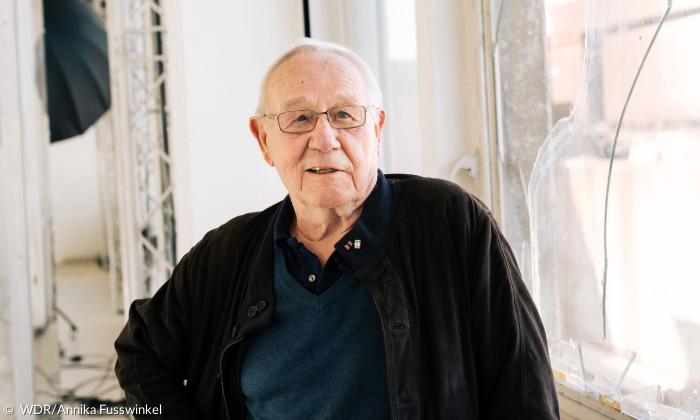 Ein älterer Mann mit weißen Haaren und Brille blickt in die Kamera
