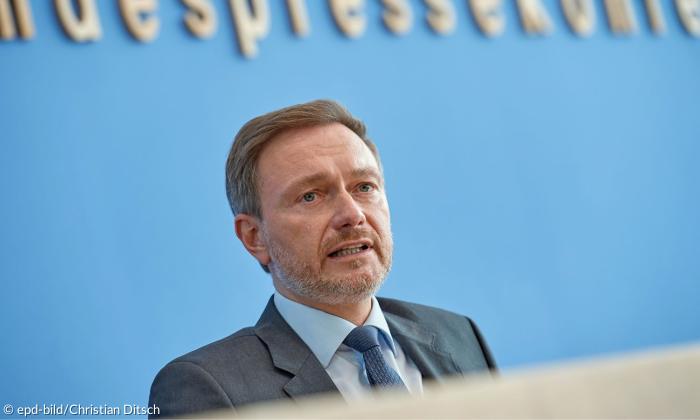 Ein Mann im Anzug mit Krawatte sitzt vor einer blauen Wand
