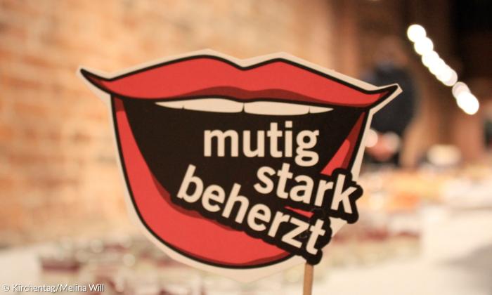 Plakat mit einem Mund, in dem das Motto des Kirchentags steht