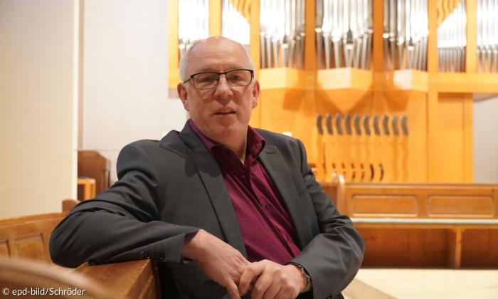 Ein Mann im Anzug sitzt in einer Kirche, hinter ihm eine Orgel