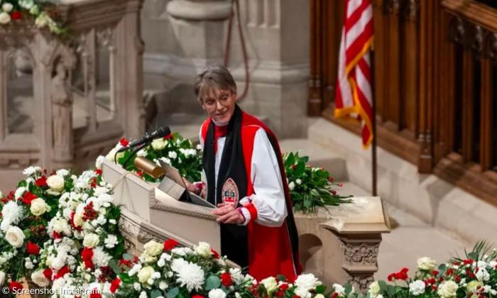 Eine Frau im Bischofsgewand steht auf einer Kanzel, hinter ihr die amerikanische Fahne, vor ihr Blumen