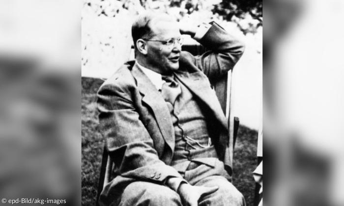 Ein schwarzweiß Bild von einem Mann, er trägt einen Anzug und hebt die linke Hand zum Kopf