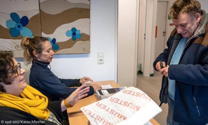 Zwei Frauen überreichen einem Mann einen Wahlzettel