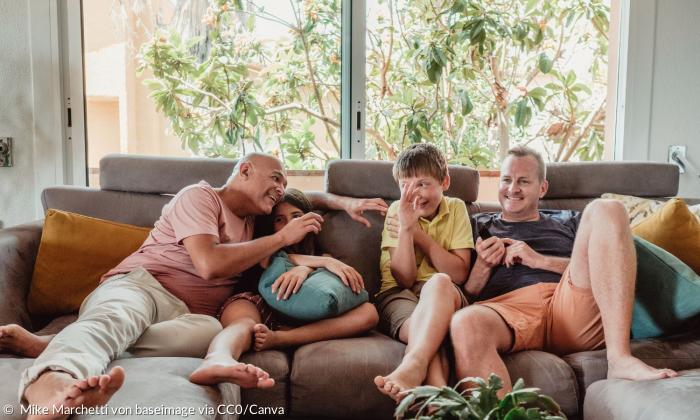 Zwei Väter mit zwei Kindern auf einem Sofa