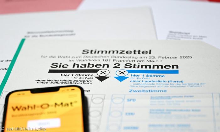 Ein Stimmzettel zur Bundestagswahl mit der Aufschrift "Sie haben 2 Stimmen". Darüber liegt ein Smartphone mit der Applikation "Wahl-O-Mat" geöffnet.