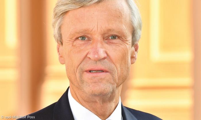 Ein Mann mit grauen Haaren und Anzug blickt in die Kamera